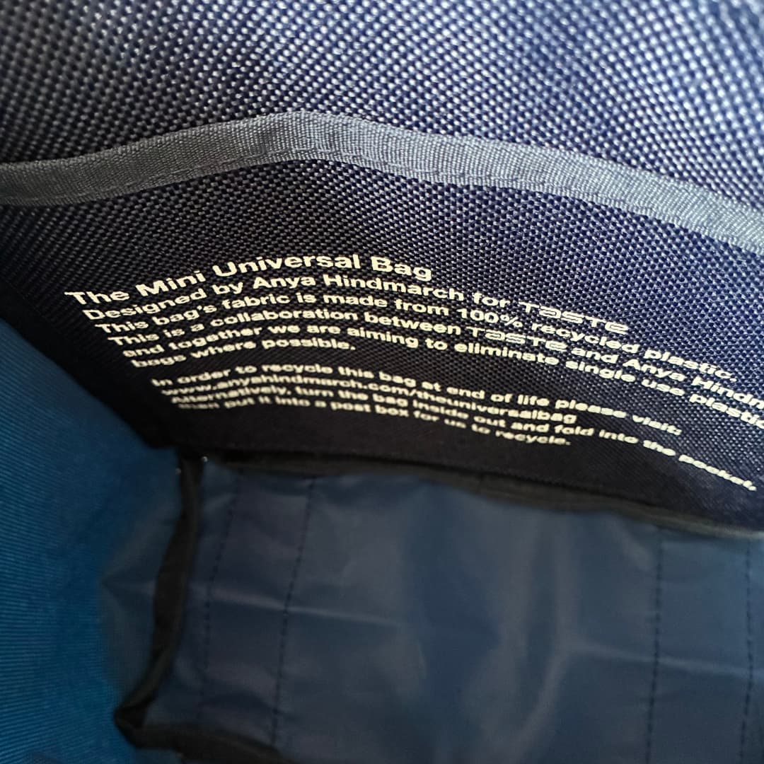 Close-up of the inside of a dark blue mini universal bag showing printed white text about recycled polyester fabric and recycling instructions.