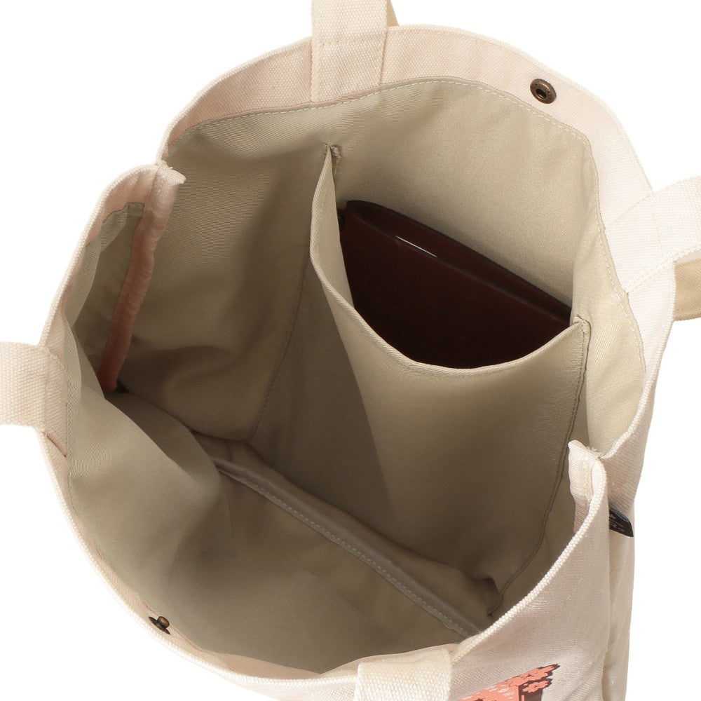 Close-up of the interior of a beige canvas tote bag, showing a central vertical organizer pocket holding a dark brown rectangular item, with a zippered compartment below and a small orange graphic near the bottom edge.