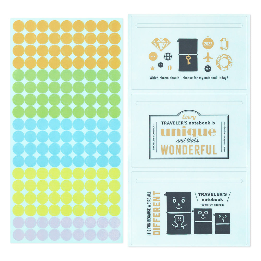 A sheet of round sticker dots in pastel rainbow colors next to a decorated notebook cover design featuring travel-themed illustrations and text.