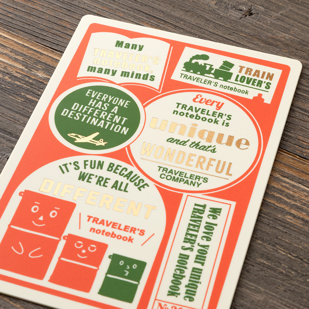 A rectangular notebook or booklet cover laid on a dark wood surface, featuring retro travel-themed graphics and text such as 'Train Lover's', 'Everyone has a different destination', and 'It's fun because we're all different'.