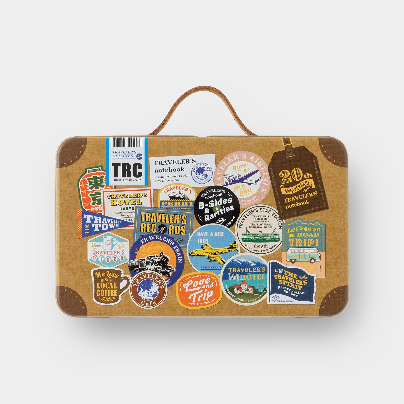 Full contents of Traveler's Notebook 20th Anniversary set laid out with tin, stickers, stamps, brass charm and history guide