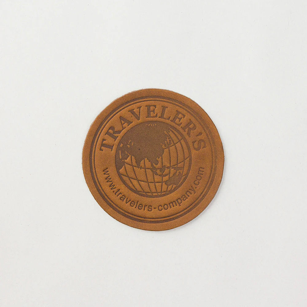 Close-up shot of the round camel leather coaster featuring the official engraved Traveler&
