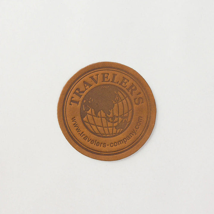 Close-up shot of the round camel leather coaster featuring the official engraved Traveler&