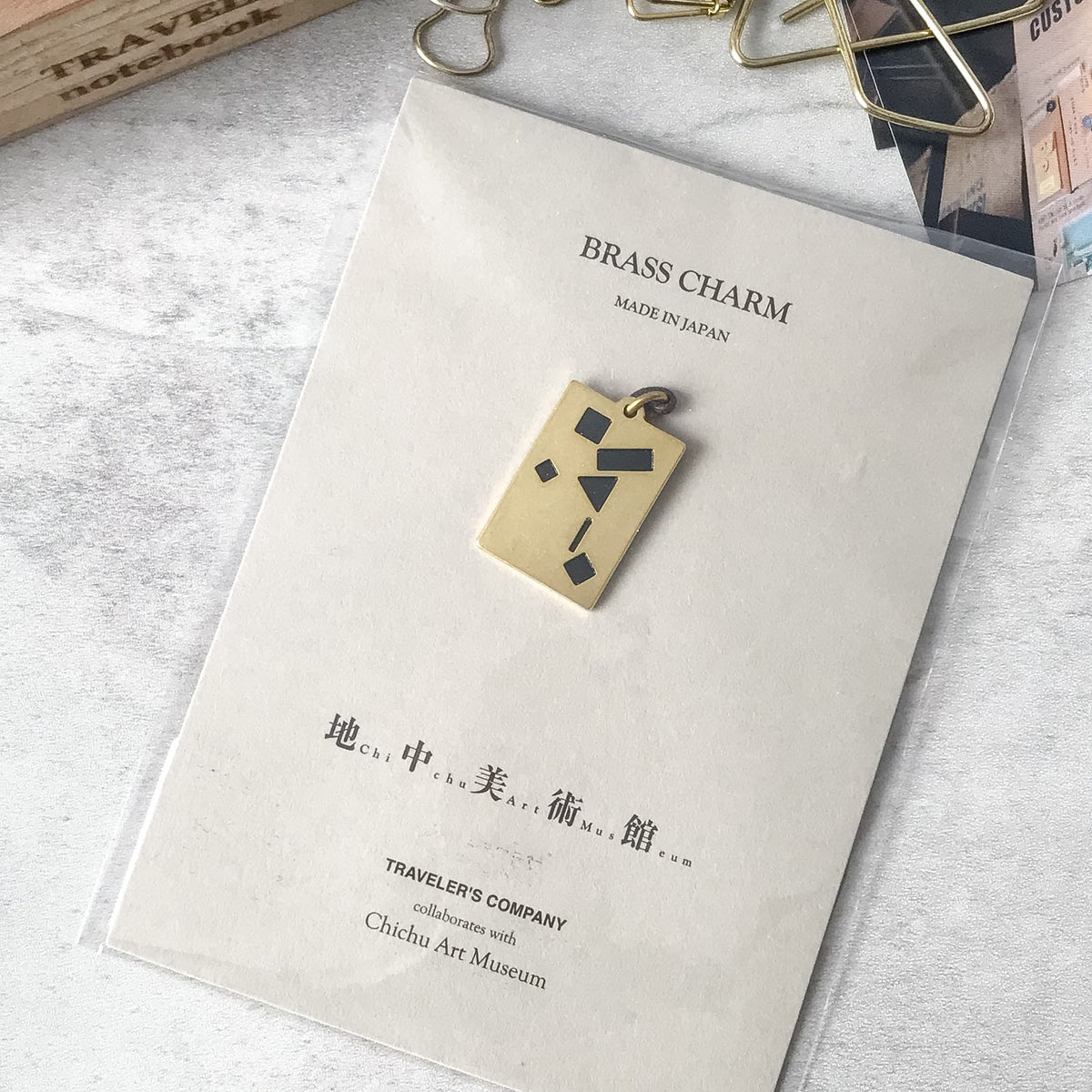 Chichu Art Museum brass charm on its display card beside stationery