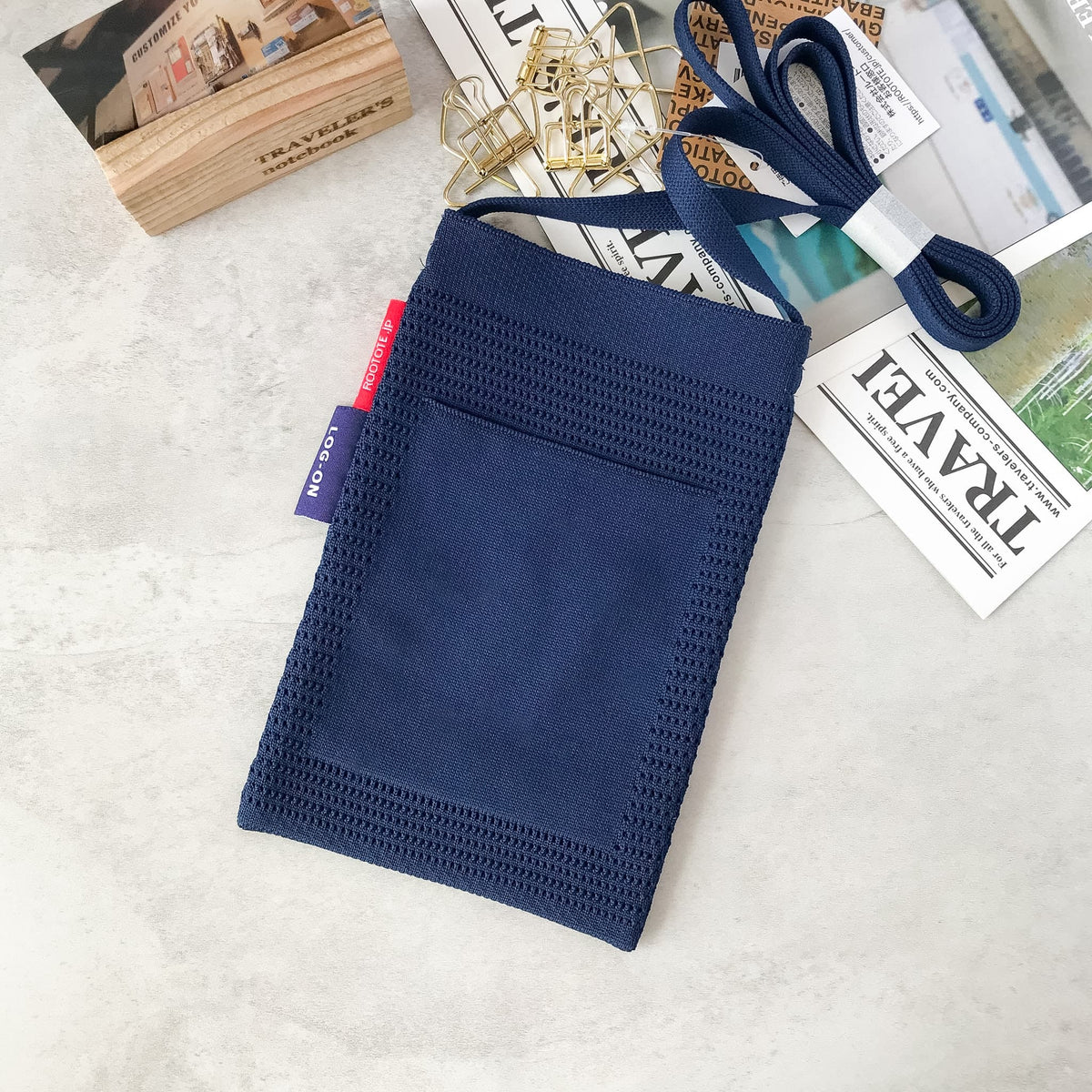 A navy blue fabric pouch or small bag with a loop strap, laid flat on a light surface with decorative books and papers around it.