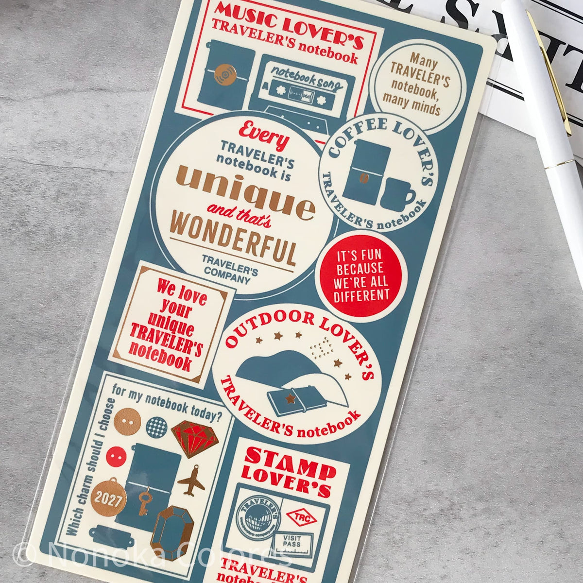 A rectangular sticker sheet featuring retro travel-themed labels and illustrations, including phrases like 'Music Lover's Notebook' and 'Coffee Lover's Notebook' on a gray stone surface.
