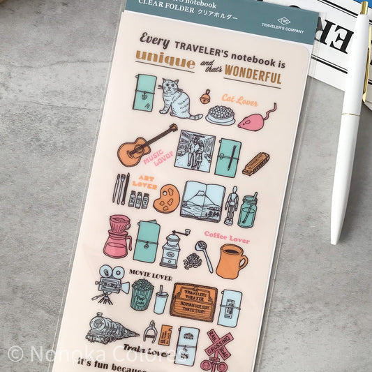 A clear folder sticker sheet from Trade Line Company featuring cute travel-themed illustrations like a cat, guitar, coffee maker, and train, with text such as 'Every TRAVELER'S notebook is unique and that's WONDERFUL'. The sheet is displayed on a gray textured surface next to a white pen.