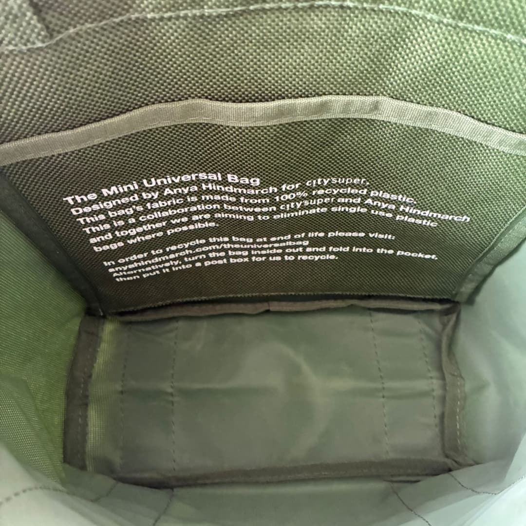 Close-up of the inside of a green fabric pouch or bag, showing printed white text on the inner lining and a padded gray-green compartment.